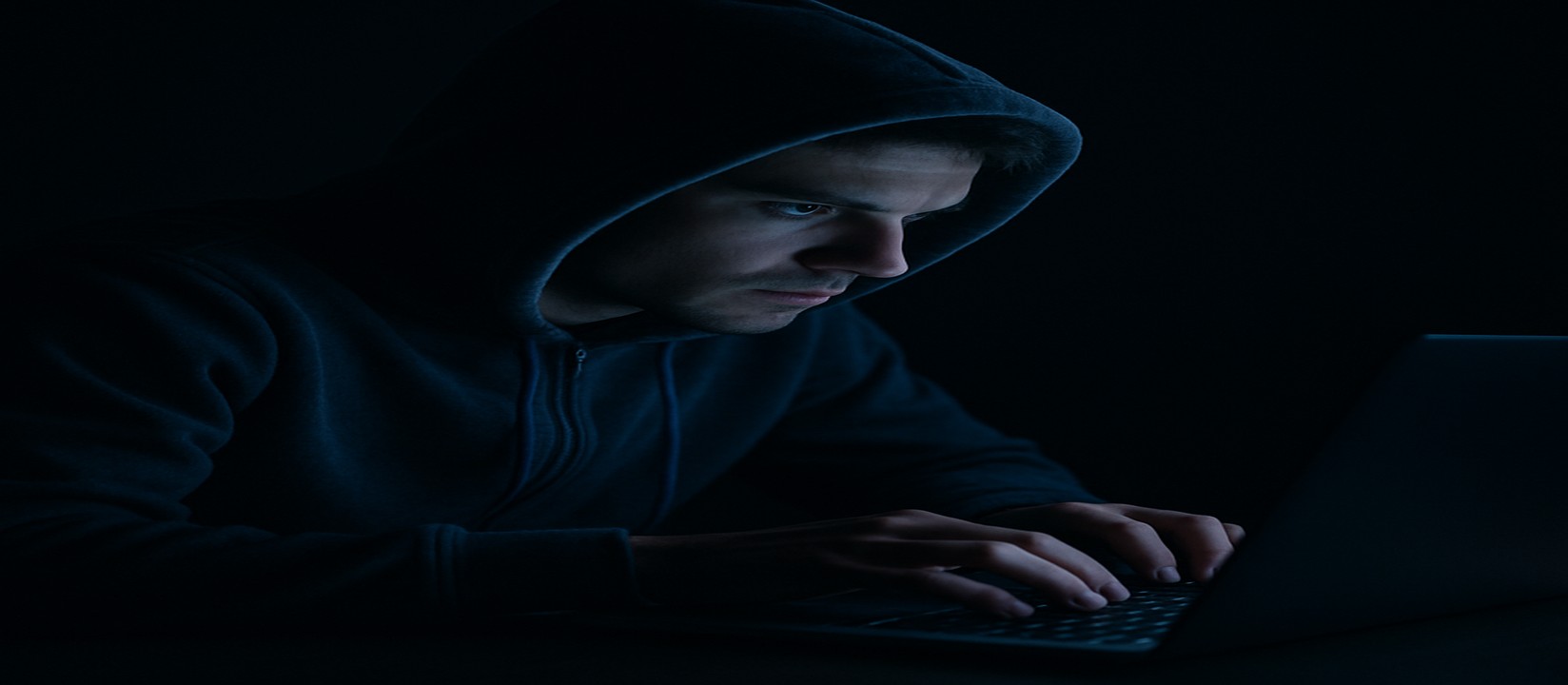 একজন ব্যক্তি অন্ধকার ঘরে ল্যাপটপে মনোযোগ স্থির করে 7777bdt ওয়েবসাইটে অনলাইন গেমিং করছেন।